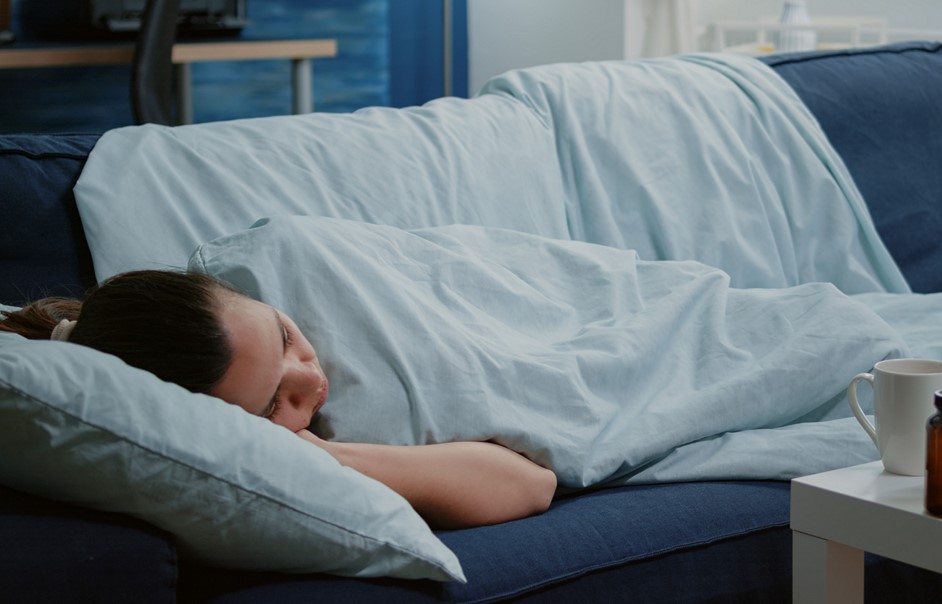Sick woman laying on couch with blanket feeling cold